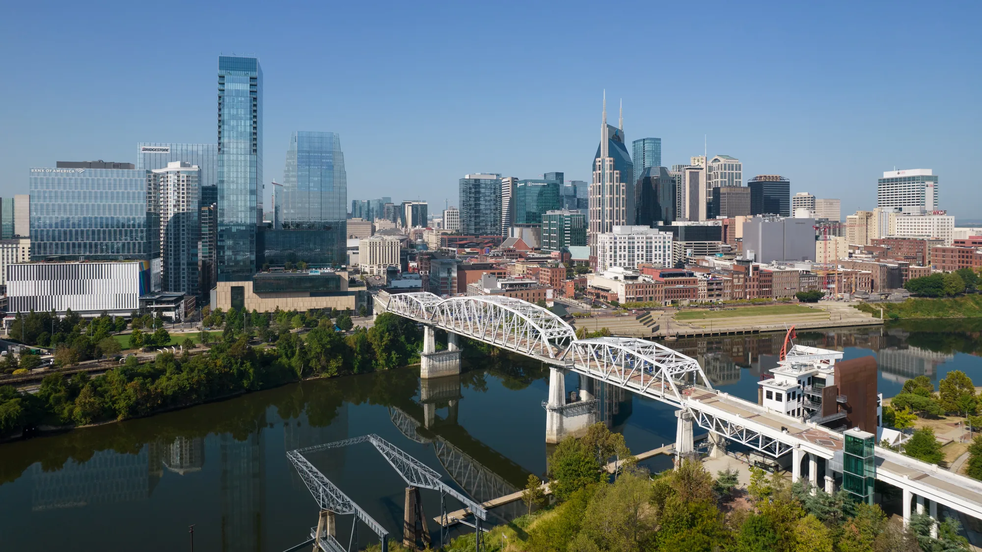 Aerial view of the white truss John Seigenthaler Pedestrian Bridge crossing the Cumberland River toward the downtown Nashville skyline